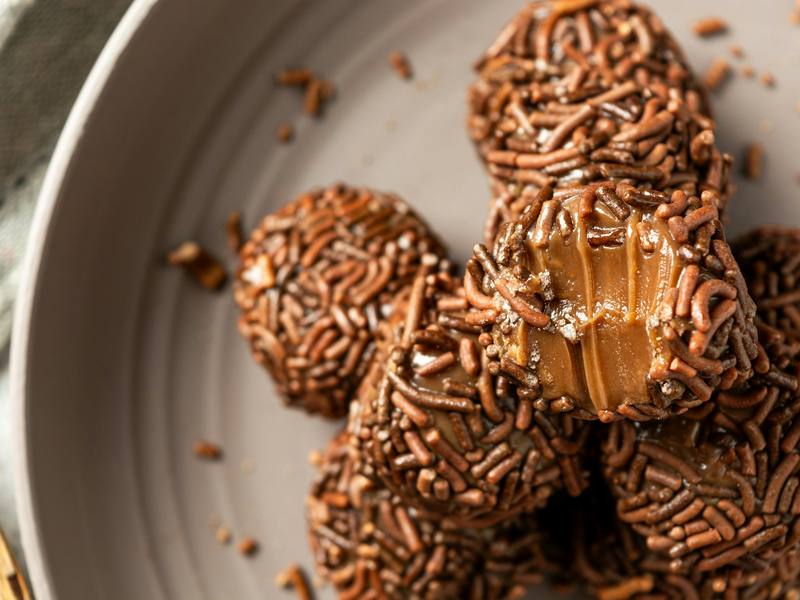 Brigadeiros cobertos de granulado, um deles mordido, em prato cinza