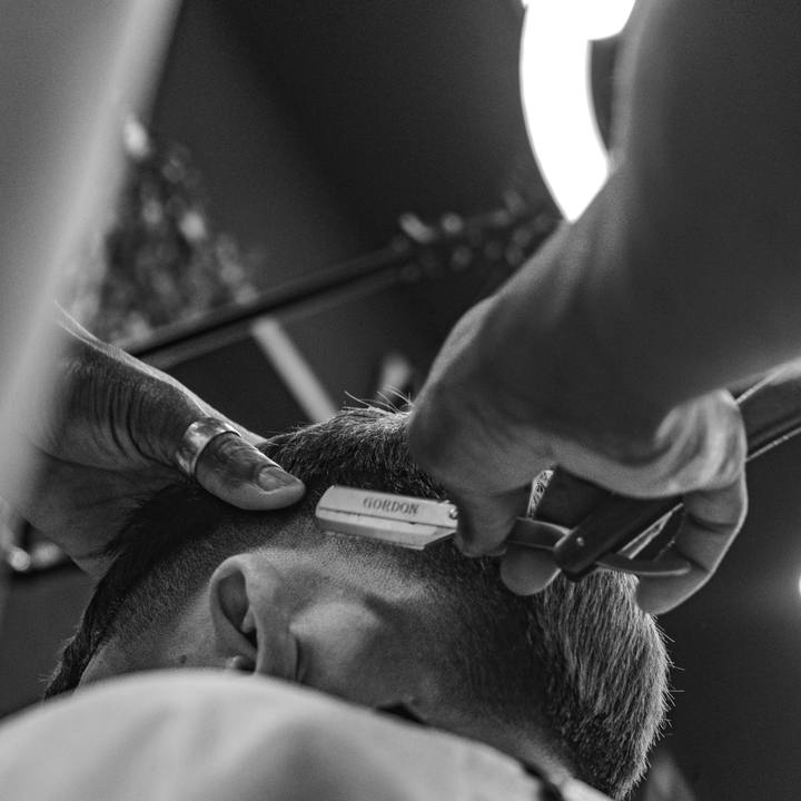 Barbeiro cortando o cabelo com tesoura, em close lateral