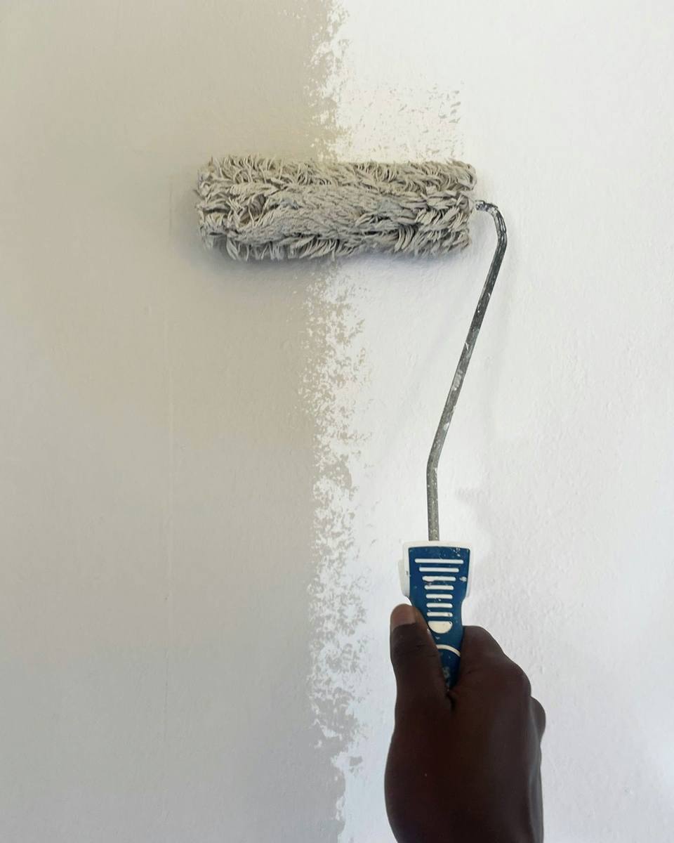 Mão aplicando tinta branca em uma parede com rolo de pintura